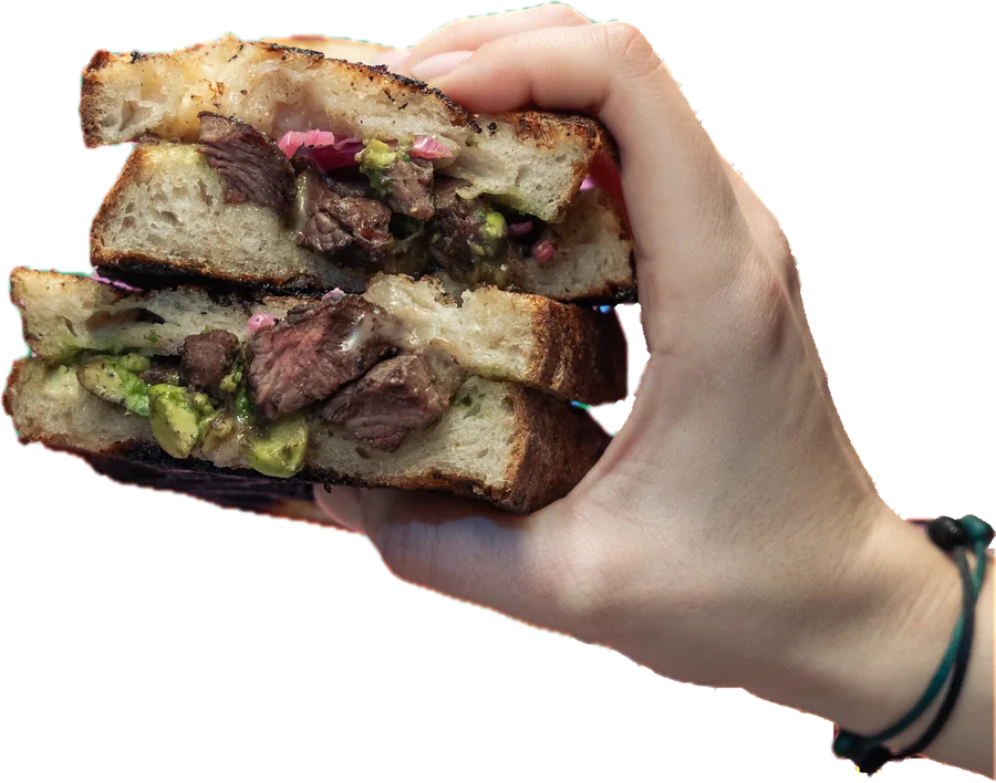 A hand holding a stacked steak sandwich with pickled onion